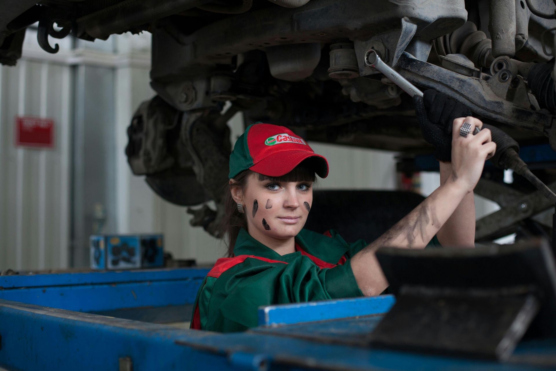 Mechanic wearing green and red uniform working under a vehicle, holding a wrench.